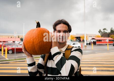 Ein Mann hält einen Kürbis nahe an sein Gesicht und lächelt auf einem Parkplatz. Hamilton, ON Stockfoto