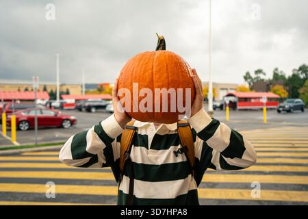 Eine Person hält einen großen Kürbis über den Kopf auf einem Parkplatz, draußen. Hamilton, ON Stockfoto