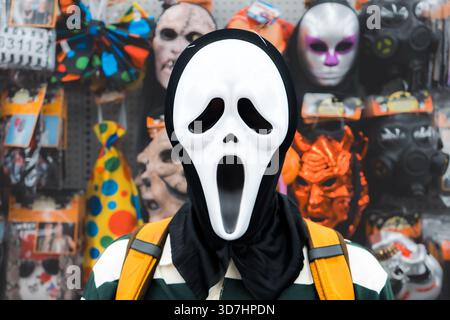 Eine Person in einer weißen Geistermaske mit anderen Masken im Hintergrund. Hamilton, ON Stockfoto
