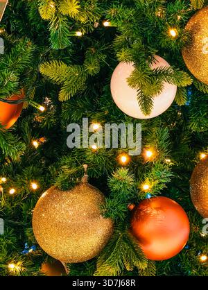 Goldene orange Weihnachtsschmuck-Kugeln auf verziertem grünen Kiefernbaum mit warmen LED-Lichtern Feiertags-festliche Winter-Dekoration Hintergrund Stockfoto