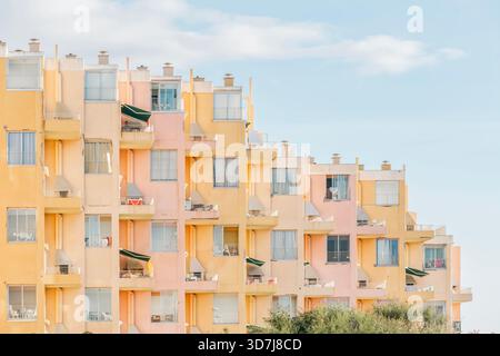 Geschwungene Fassade eines großen Appartements oder Hotelgebäudes mit Balkonen in Pastellrosa und Gelb unter einem weichen Sommerhimmel Stockfoto