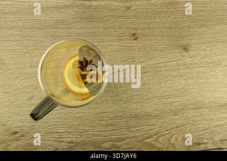 Sternanis, Zimtstangen, Tee und ein in Scheiben geschnittenes ​​orange in einem leeren Glas auf einem Holztisch, Zutaten für einen warmen Wintertee Stockfoto