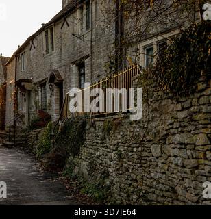 Traditionelle Steinhäuser mit Eisengeländern in einer ruhigen, engen Straße, gesäumt von moosbedeckten Wänden und Herbstlaub Castle Combe UK Stockfoto