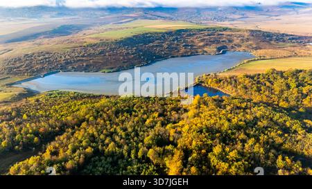 Drohnenblick auf den Bârca-See in der Nähe von Iași, Rumänien, am frühen Morgen. Ruhiges Wasser, Nebel und herbstliche Farben schaffen eine friedliche Landschaft. Stockfoto