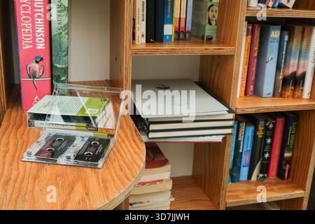 Alte Tonkassette, die zwischen Papierbüchern auf hölzernem Bücherregal liegt. 12. Oktober 2025, Lunz am See, Österreich. Stockfoto