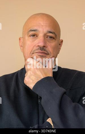 Glatzkopf, der sein Kinn auf seiner Hand in einer nachdenklichen Pose vor neutralem Hintergrund legt. Stockfoto
