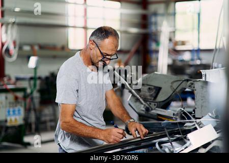 Fabrikarbeiter, der Metallwerkstoffe in der industriellen Werkstatt untersucht und dabei Qualitätskontrollen, Inspektionen und Fertigungsprozesse vertritt. Stockfoto