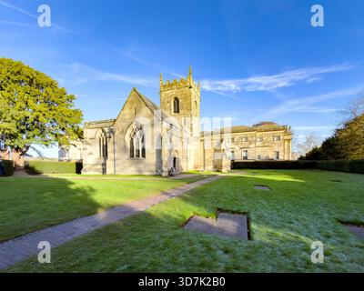 All Saints' Church in Kedleston, Derbyshire, mit Bogenfenstern und Glockenturm, umgeben von grünem Rasen und Bäumen unter klarem blauem Himmel Stockfoto