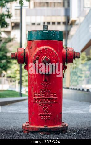 Eine Nahaufnahme eines verwitterten roten Feuerhydranten mit grüner Spitze in der Innenstadt von Montreal, aufgenommen vor einer städtischen Kulisse aus modernen Gebäuden und weichen Stockfoto