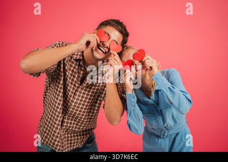Glückliches Paar hält fröhlich rote Herzformen auf spielerische Art und Weise und zeigt ihre Liebe und Zuneigung zueinander in einem unterhaltsamen Moment Stockfoto
