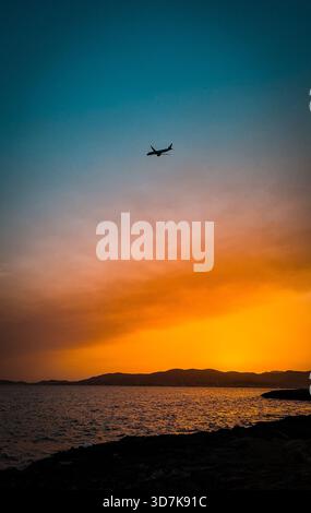 Flugzeugsilhouette fliegt über dem Meer vor einem leuchtenden orange-blauen Sonnenuntergang Himmel auf Mallorca Stockfoto