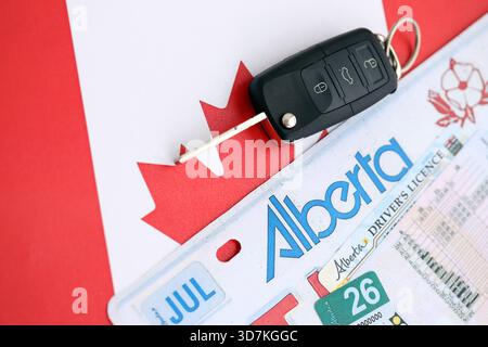 Alberta canadian Autokennzeichen und Zündschlüssel auf der Flagge von Kanada Nahaufnahme. Führerschein- und Zulassungskonzept Stockfoto