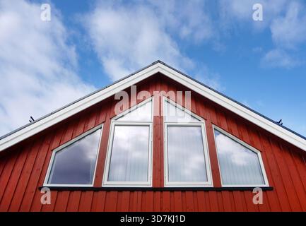 Architektonische Details. Flacher Blick auf eine rote Holzdachkonstruktion im skandinavischen Stil. Fassade eines Hauses mit großen geometrischen Fenstern re Stockfoto