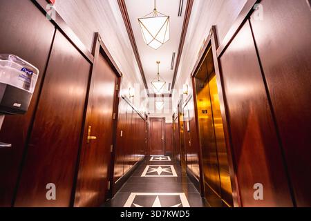 Eleganter Aufzug-Flur mit Holztäfelung, geometrischer Beleuchtung und poliertem Boden. Stockfoto