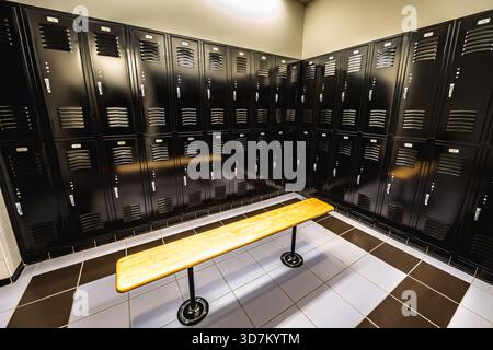 Moderner Umkleideraum mit schwarzen Metallschränken und einer Holzbank. Stockfoto