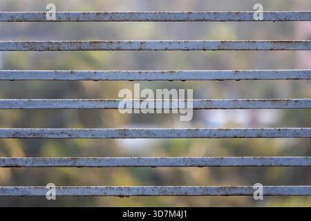 Nahaufnahme eines alten, korrodierten Edelstahlbalkongeländes und Zauns im Kontrast zu einem schönen, weichen Naturhintergrund im Freien (boke Stockfoto