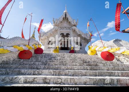 Dok KHAM TAI, THAILAND - 20. NOVEMBER 2025: Ordinationshalle im Sri Chum Tempel in der Provinz Phayao, mit Nagagatreppen, Regenschirmen und Bannern Stockfoto