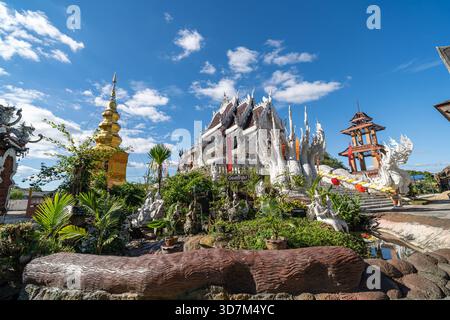 Dok KHAM TAI, THAILAND - 20. NOVEMBER 2025: Weiße Ordinationshalle mit Nagatreppen, üppigem Garten und goldenen Chedi im Sri Chum Tempel in Phayao provi Stockfoto