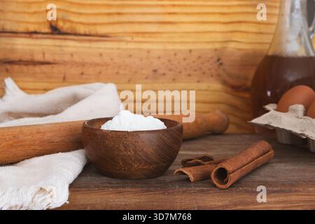 Ein rustikaler Holztisch mit Backzutaten wie Mehl, Zimtstangen, einer Nudelnadel und Eiern für die Zubereitung eines hausgemachten Rezepts. I Stockfoto
