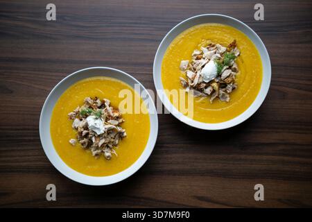 Eine Schüssel Kürbiscremesuppe mit gehacktem Huhn und Sahne steht auf einer dunklen Holzoberfläche. Stockfoto