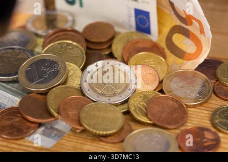 Berlin, Deutschland. November 2025. Auf einem Tisch befinden sich Münzen verschiedener Euro-Stückelungen, darunter ein- und zwei-Euro- und Cent-Stücke. Teile der Euro-Banknoten sind im Hintergrund zu sehen. Quelle: Fernando Gutierrez-Juarez/dpa/Alamy Live News Stockfoto