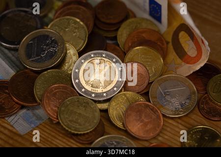 Berlin, Deutschland. November 2025. Auf einem Tisch befinden sich Münzen verschiedener Euro-Stückelungen, darunter ein- und zwei-Euro- und Cent-Stücke. Teile der Euro-Banknoten sind im Hintergrund zu sehen. Quelle: Fernando Gutierrez-Juarez/dpa/Alamy Live News Stockfoto