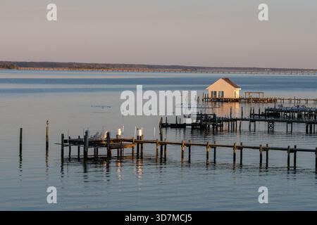 Ruhige Herbstszene auf dem Rappahannock River während der goldenen Stunde. Hölzerne Docks und ein kleines Bootshaus stehen vor dem ruhigen Wasser, mit Reflexionen Stockfoto