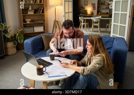 Kaukasischer Mann mittleren Alters und kaukasische junge Erwachsene Frau, die Finanzdokumente überprüfen und gemeinsam zu Hause Laptop benutzen, Steuerformulare vorbereiten und Ausgaben für Steueranträge berechnen Stockfoto