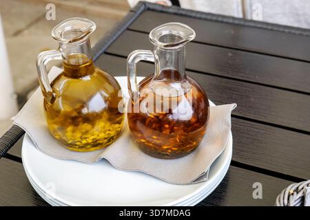 Zwei Glasbrocken mit Knoblauch- und Chili-Olivenöl auf einem Restauranttisch, goldene und bernsteinfarbene Öl-Würzflaschen auf Teller mit Serviette, Mediter Stockfoto