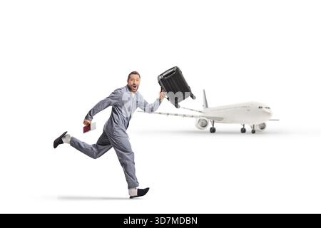 Mann im Pyjama, der mit Koffer und Pass am Flughafen auf weißem Hintergrund läuft Stockfoto