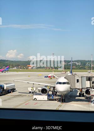 Generisches Passagierflugzeug am Gate mit Jet Bridge Laufsteg befestigt Fuel Truck Bodenbesatzung bereitet Flugzeuge für den Abflug sonnige Tagesregion vor Stockfoto