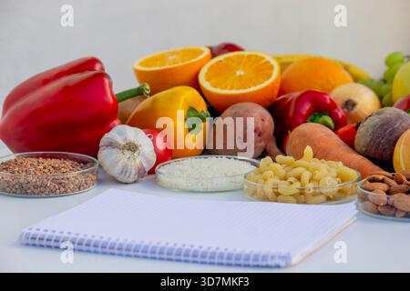 Leerer Notizblock zum Schreiben eines Diätplans vor dem Hintergrund von Obst, Gemüse und Getreide. Stockfoto