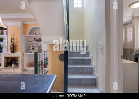 Helle Treppe mit Marmortreppen, schmiedeeisernem Geländer und teilweiser Blick auf Kamin und Regale Stockfoto