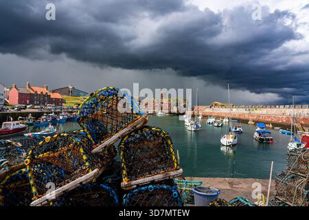 Sturmwolken über Dunbar Hafen mit Fischkreelen im Vordergrund Stockfoto