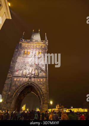 Historischer gotischer Turm der Karlsbrücke, beleuchtet bei Nacht mit Touristenmassen in Prag Stockfoto