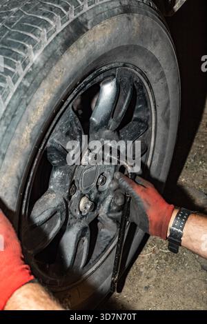 Ein Mechaniker zieht die Radmuttern mit einem Radmutternschlüssel an einer Nabe fest. Ein Rad an einer Autoachse montieren und ausbauen. Stockfoto