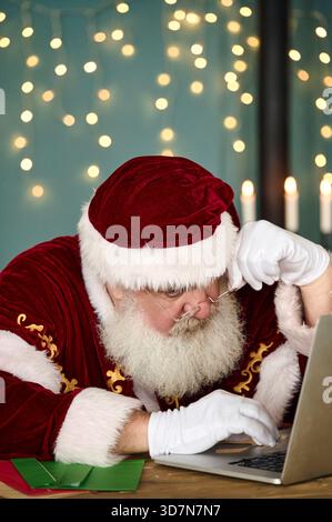 Der Weihnachtsmann liest Kinderbriefe auf dem Computer und bestellt online Stockfoto