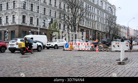 Arbeiter reparieren die Fahrbahn, während Fahrzeuge um Bauschranken fahren. Kiew, Ukraine, 26. November 2025. Stockfoto