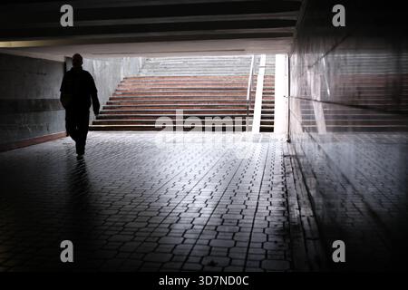 Eine Einzelfigur läuft durch einen dunklen Tunnel zu einem weichen Licht draußen. Stockfoto