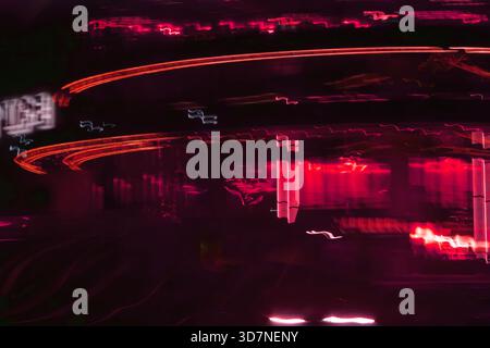 Eine stimmungsvolle und verschwommene Aufnahme der Lichter der Stadt in einer regnerischen Nacht mit wunderschönen Reflexionen auf einer nassen Oberfläche. Stockfoto