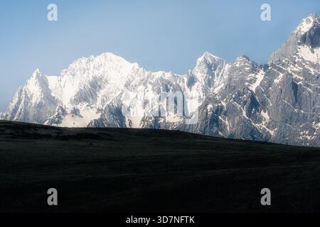 Aus der Vogelperspektive auf schneebedeckte Berge, die den Himmel durchdringen, deren zerklüftete Gipfel im Kontrast zum dunklen Vordergrund stehen, Lijiang, China. Stockfoto