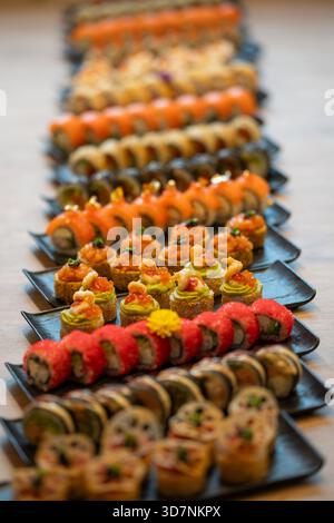 Eine lebendige Auswahl an verschiedenen Arten von Gourmet-Sushi und Maki-Rollen mit verschiedenen Geschmacksrichtungen und künstlerischen Darstellungen ist auf schwarzem Pl angeordnet Stockfoto