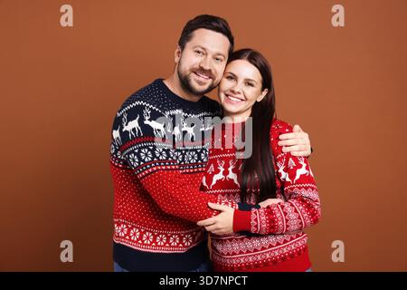 Glückliches Paar in Weihnachtspullover auf braunem Hintergrund Stockfoto