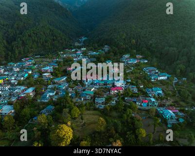 Blick aus der Vogelperspektive auf ein malerisches Dorf, eingebettet in die Ausläufer von grünen Bergen, ein Flickenteppich von Dächern, die im Kontrast zum dichten Wald stehen, Bir, Himacha Stockfoto