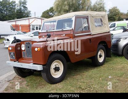 Brauner Vintage Land Rover Series IIA mit Segeltuch, das bei einer Autoveranstaltung mit anderen Fahrzeugen im Hintergrund auf Gras geparkt wurde Stockfoto