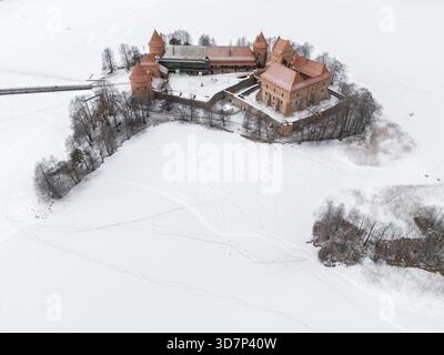 Blick aus der Vogelperspektive auf die mittelalterliche Burg Trakai mit ihren markanten roten Ziegeln vor der riesigen Weite des weißen Schnees, Trakai, Litauen. Stockfoto