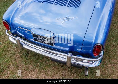Rückansicht eines klassischen blauen Volkswagen Karmann Ghia, der auf Gras geparkt ist, mit Chromstoßfänger und Vintage-Nummernschild Stockfoto