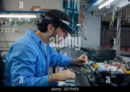 Techniker Mann Löttechniker in einem blauen Labormantel repariert einen Laptop sorgfältig Stockfoto