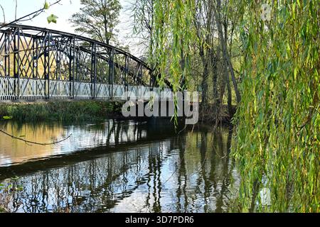 Metallbrücke über den Fluss mit Reflexionen und hängenden Weidenzweigen Stockfoto
