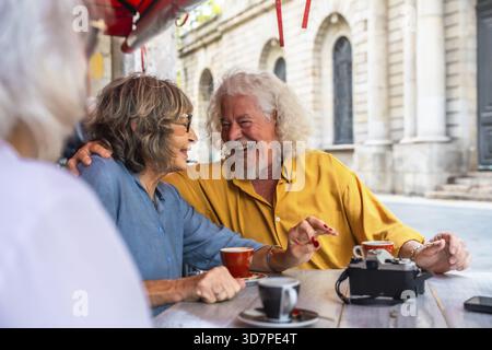 Seniorenfreunde teilen einen Moment der Freude und des Lachens, während sie einen Kaffee in einem Café im Freien genießen, in dem sie Glück, Freundschaft und einen lebendigen aktiven Seni verkörpern Stockfoto